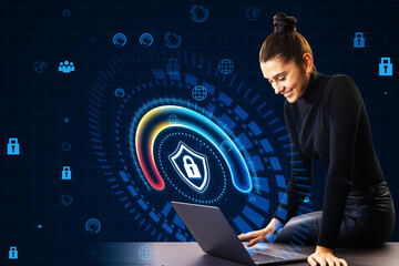 Happy young businesswoman sitting on desk and using laptop with glowing round padlock shield...