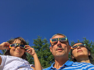 Mother, father and daughter looking at the sun during a solar eclipse on a country park, family outdoor activity - 756985323