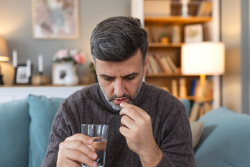 Man takes medication prescribed by his physician. Man taking a pill and drinking a glass of water....