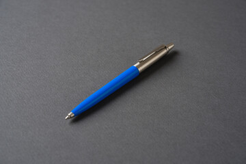 Blue plastic and metal ballpoint pen on dark gray background