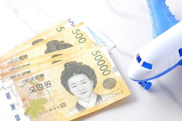 韓国の通貨、ウォンKRWの紙幣と飛行機で、韓国旅行のイメージ
