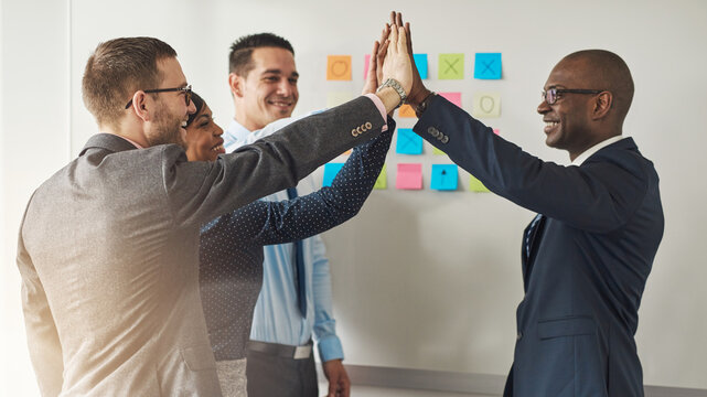 Diverse business colleagues giving high five to each other standing in a office boardroom. Team members celebrating and enjoying success at work by giving high five.