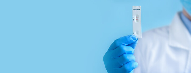 A doctor wearing a protective mask and gloves shows a rapid laboratory test for Disease X test . The test shows a positive result. Virus diagnosis, inhibition of disease outbreaks. Banner. Copy space
