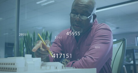 Image of numbers and data processing over african american businessman working in office