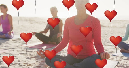 Image of red heart balloons, over women exercising on beach
