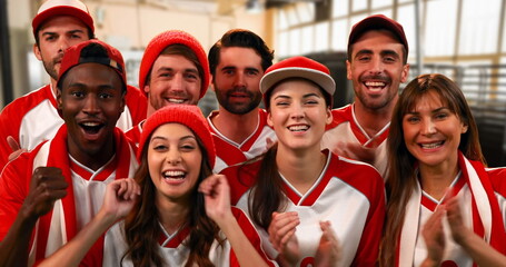 Front view of a group of sports fans wearing red and white jerseys lively cheering