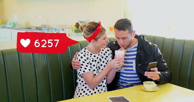 Couple shares shake and browses phone by a heart icon tally at dinner. - Powered by Adobe