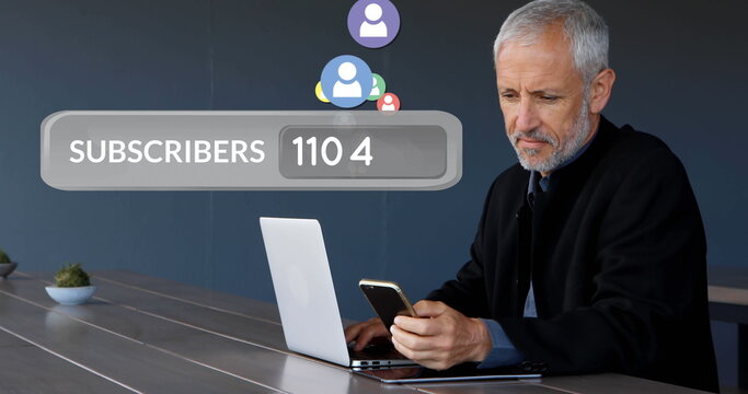 Close up of a Caucasian old man browsing on his phone in front of his laptop