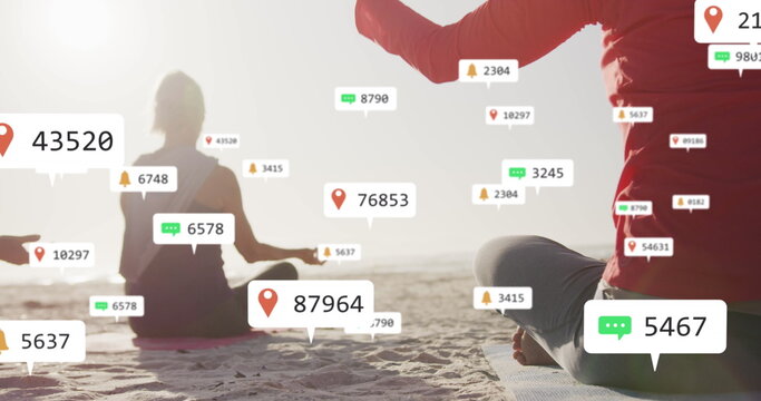Image of social media notifications, over women doing yoga sitting on beach
