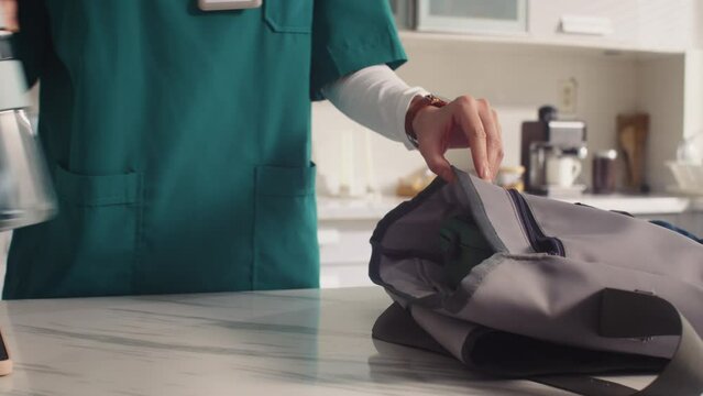 Vertical shot of medical worker in uniform putting lunch box in bag before work