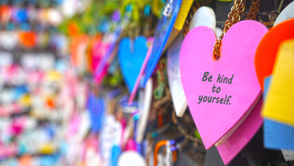 Colorful hearts on the street hanging on wall with text message - Be kind to yourself. Self love and care concept. Inspirational and self motivational quotes.
