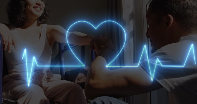 Image of neon heart rate and heart over happy biracial couple, woman on wheelchair - Powered by Adobe