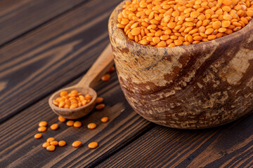 Photo of red lentils in wooden bowl with wooden measuring cup on wooden background.  Healthy lifestyle. Vegetarian and vegan diet.