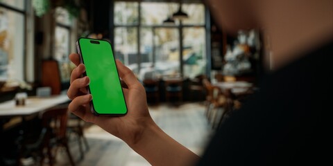 Person holding a smartphone with a green screen in a blurred cafe setting - 757020901