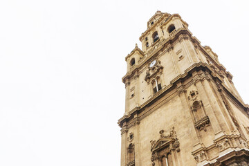 Fototapeta premium Murcia cathedral background. Rainy day white sky. Traveling around Spain. Cityscape spanish architecture. Cathedral de Santa Maria tower with clock.