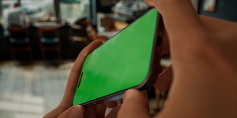 Person holding a smartphone with a green screen in a blurred cafe setting - 757024151
