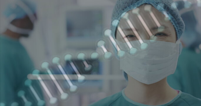 Image of dna strand over portrait of smiling asian female surgeon in operating theatre