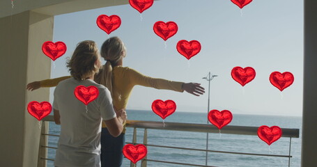 Image of social media red heart balloons over couple in love on balcony by seaside