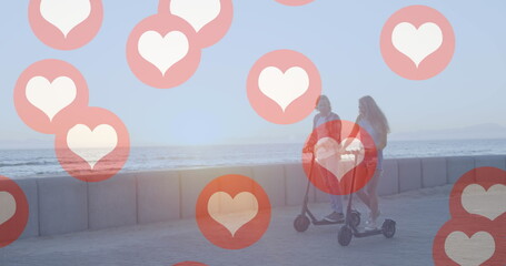 Image of social media red heart icons over couple on electric scooters by seaside