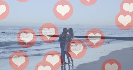 Multiple red heart icons floating against caucasian couple kissing on the beach