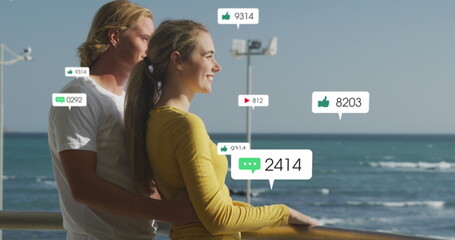 Image of social media icons over happy couple by seaside