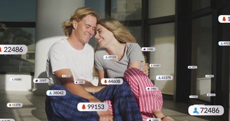 Image of social media notifications over smiling couple relaxing indoors in the sun