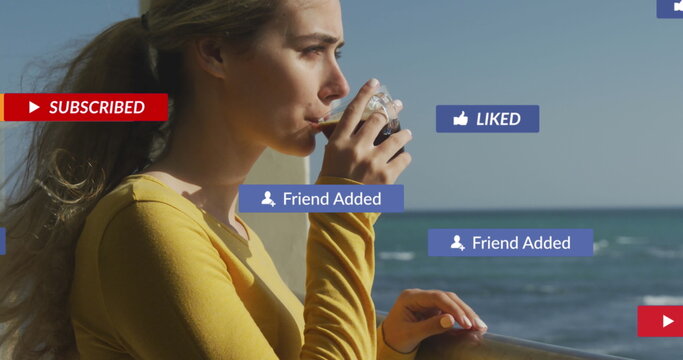 Image of social media notifications over woman on holiday drinking coffee by the sea