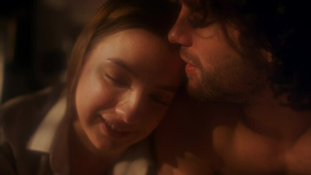 Close up shot of young happy couple in love chatting, smiling and kissing in dark bedroom with warm light