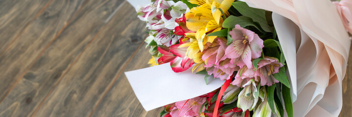 banner of bouquet from multi-colored flowers with empty card or note on the wooden background. multicolored alstroemerias, pink, yellow, purple, white and red alstroemerias. Soft focus