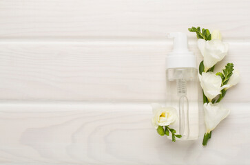 Fototapeta na wymiar Cosmetic bottle with freesia flowers on wooden background, top view