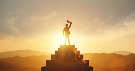 Silhouette of businessman holding a trophy on top staircase with light sunset. concept of a...