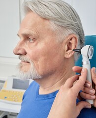 Elderly man while ear test with audiologist with otoscope at medical office, close-up. Diagnosis of hear impairment, check-up, otoscopy