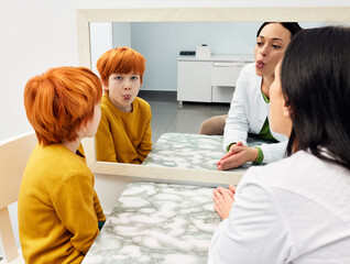 Speech training. Boy doing tongue exercises with his speech therapist near large mirror for correct pronunciation