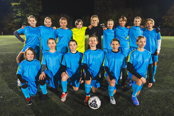 full shot of a school-age girls' team taking a picture with their woman coach at a practice at night. High quality photo