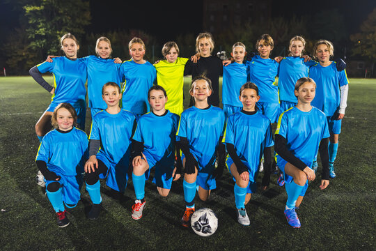 full shot of a school-age girls' team taking a picture with their woman coach at a practice at night. High quality photo