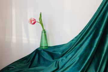 pink tulips in green glass vase on background green velvet clothes