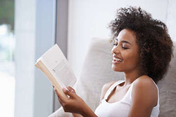 Happy, black woman and reading with book on couch for novel, story or literature in living room at home. African female person with smile for information, news or interesting knowledge at the house - obrazy, fototapety, plakaty