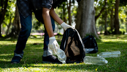 Hand holding plastic bottle waste, picking up trash and putting it in the black garbage bag at the...