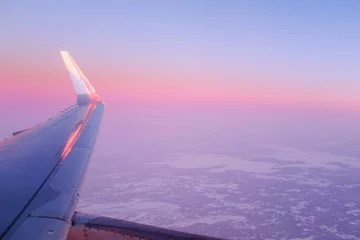 Foto op Plexiglas Airplane flying over a snowy landscape in Rovaniemi, Finland on a beautiful cloudy sunset sky with aircraft wing © jordieasy