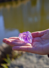 A close up image of a hand holding a purple amethyst crystal stone - semiprecious gem used in esoteric and alternative medicine.