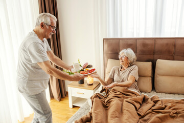 A caring senior man is bringing breakfast in bed to his wife.