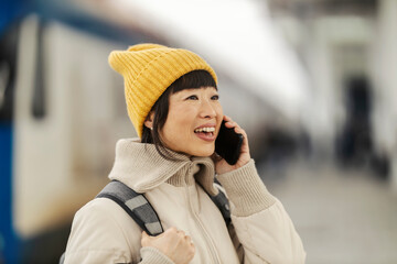 Portrait of a happy japanese traveler standing at train station and talking on her phone.
