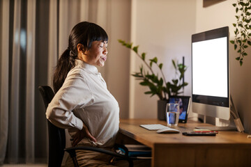An asian businesswoman is sitting at home office and night and having back pain.