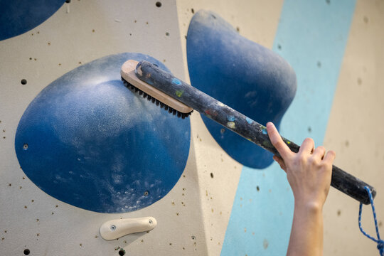 Hand holding big brush on long stick in bouldering climbing gym brushing off chalk of a large hold for the hands