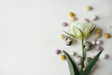Stylish easter eggs and tulip on rustic white table. Happy Easter! Easter flat lay. Modern natural dye marble and candy chocolate eggs with spring flower border. Space for text