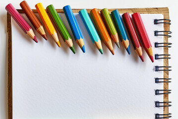 Fototapeta premium ketchbook and colored pencils on a white background, isolated image, photo, Backgrounds for school, backgrounds for kindergarten, children's backgrounds
