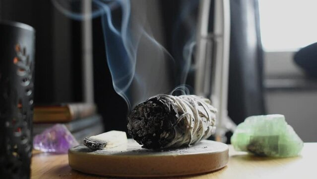 A close up image of a burning white sage smudge stick and healing crystals. Witchcraft, meditation, healing sage.