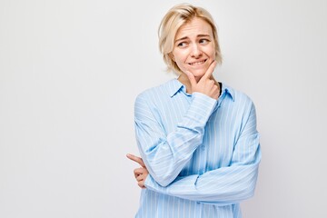 Woman with thoughtful expression, touching chin, wearing a blue shirt against a white background.