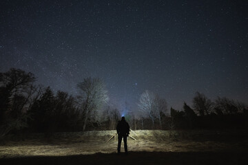 Night scene, landscape astrophoto, Estonian nature. A man with a headlamp in a field.
