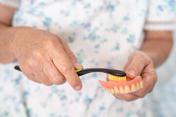 Asian elderly woman patient use toothbrush to clean partial denture of replacement teeth.